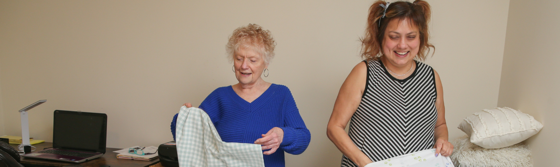 Senior woman and caregiver helping fold towels