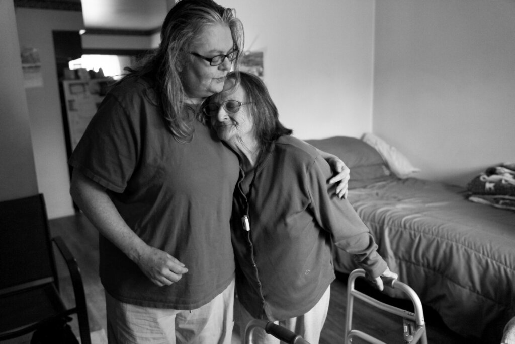 Older woman with walker leaning into another woman.